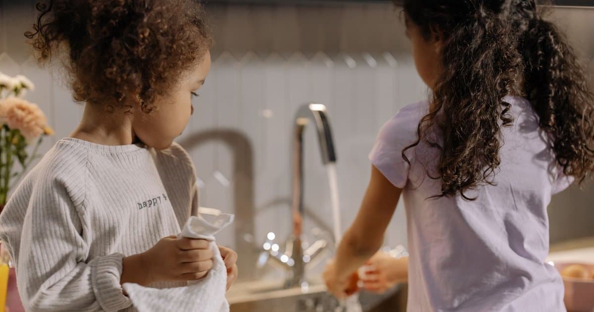 Two girls washing dishes together in a kitchen, illustrating sibling collaboration and leadership skills.