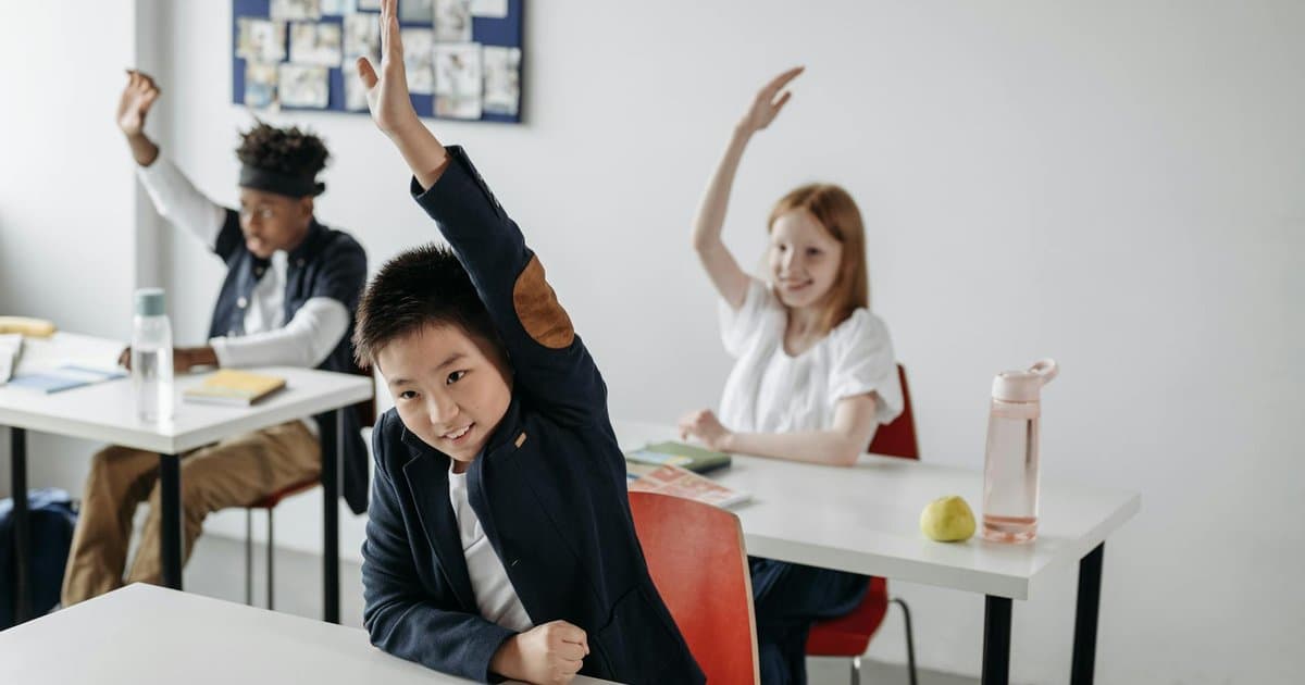 Children raising hands in a classroom during a lesson, building confidence through class participation.