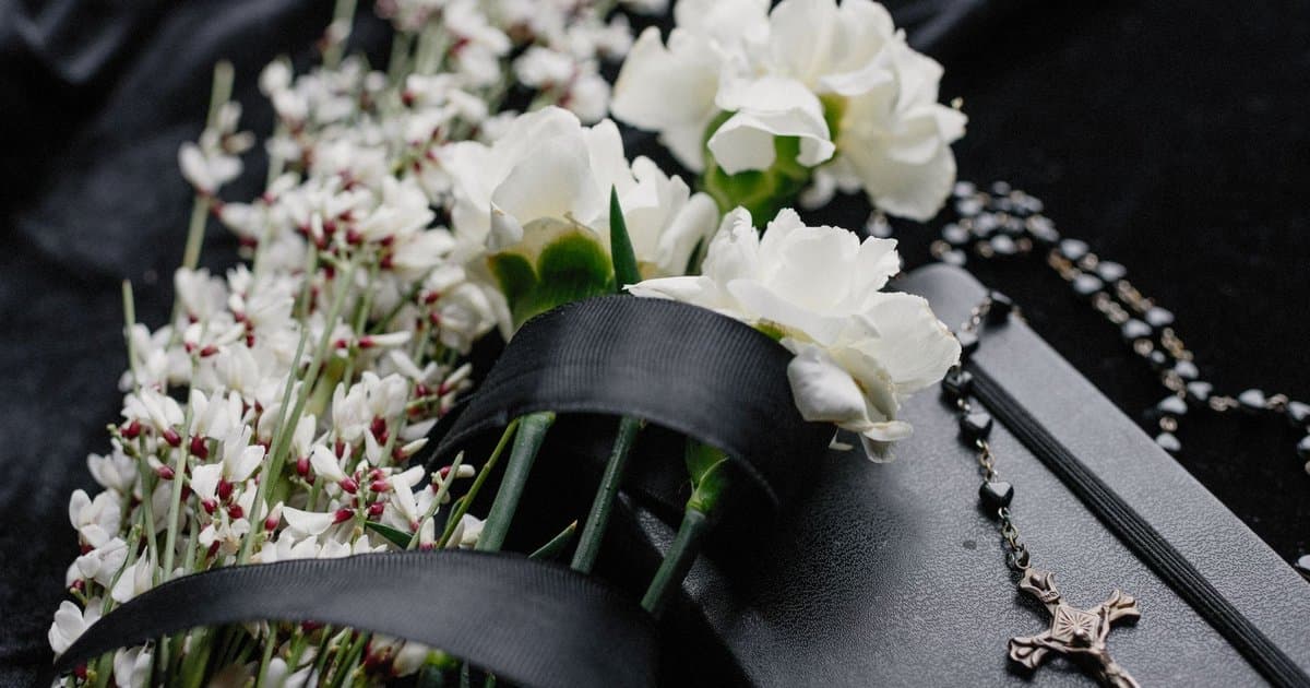 White flowers and rosary beads on dark cloth, representing memorial symbols for creating a cat tribute book.