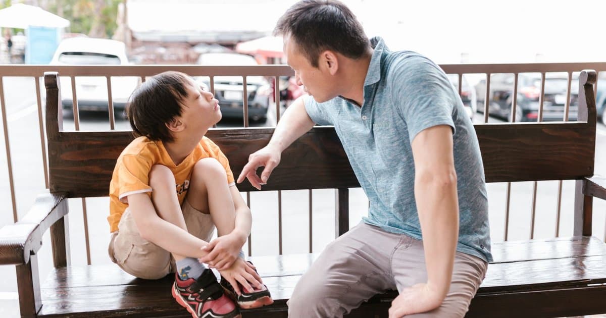 Father and son sitting on a wooden bench outdoors, maintaining emotional connection across family transitions.