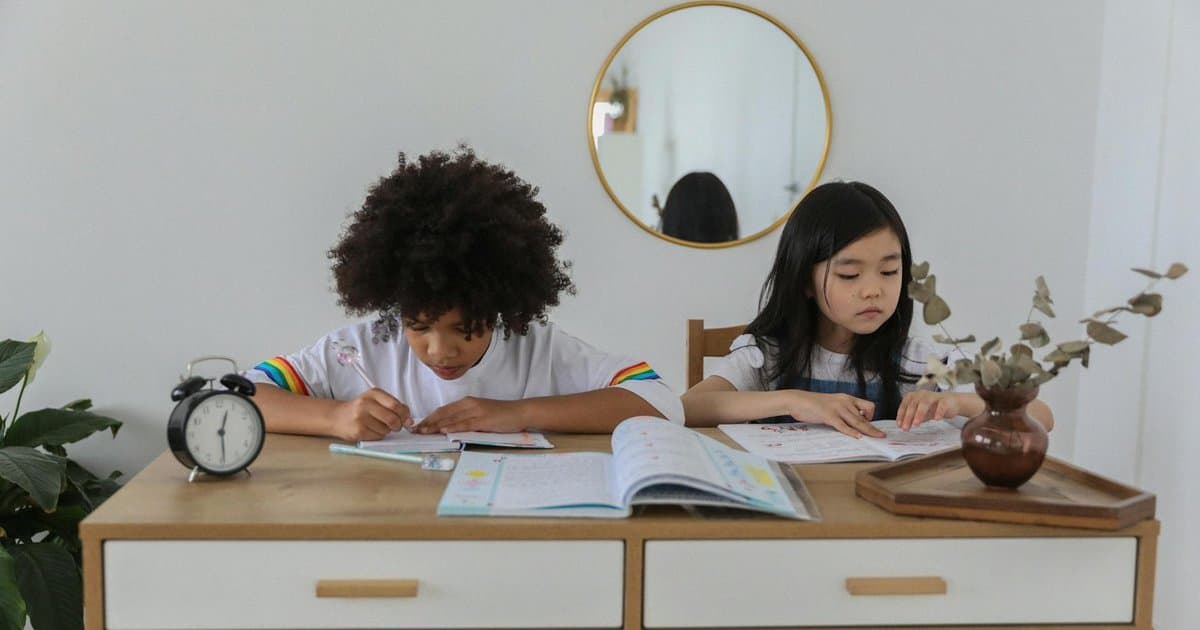 Two girls writing in notebooks at a table with holiday decorations visible in background.