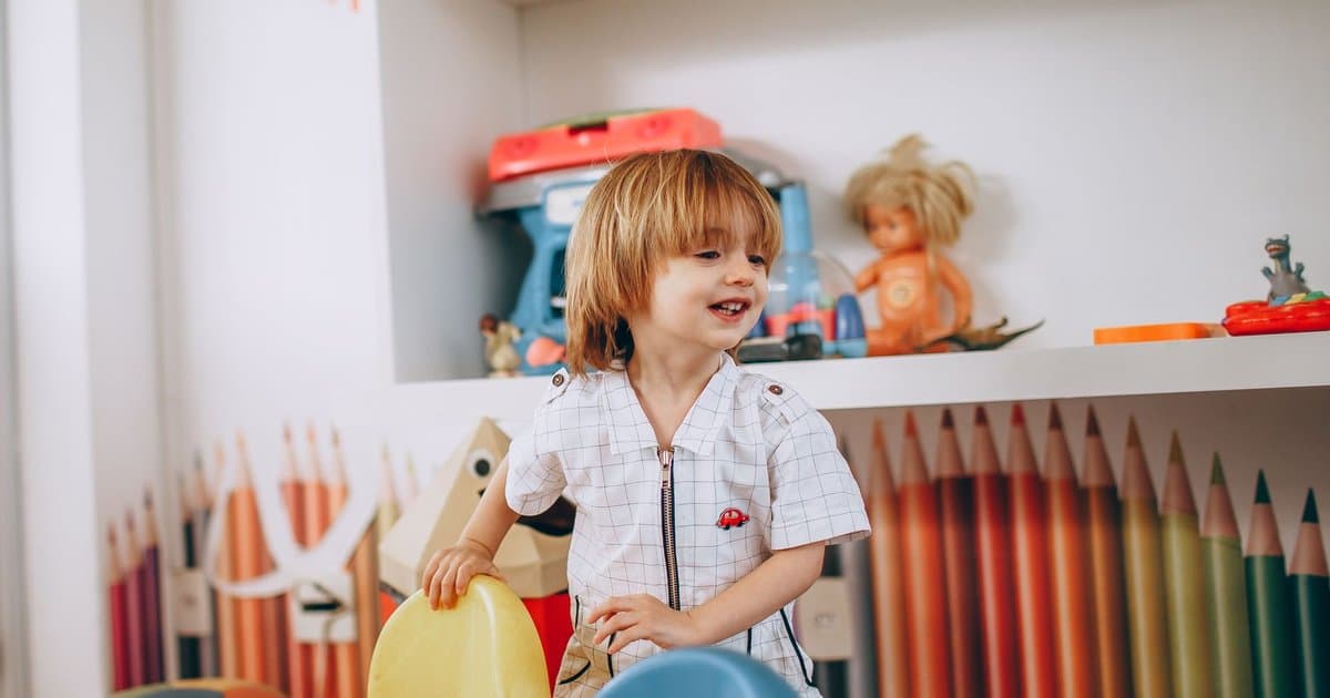 A smiling child plays in a colorful preschool classroom, demonstrating the kind of structured routine visual schedules help support.