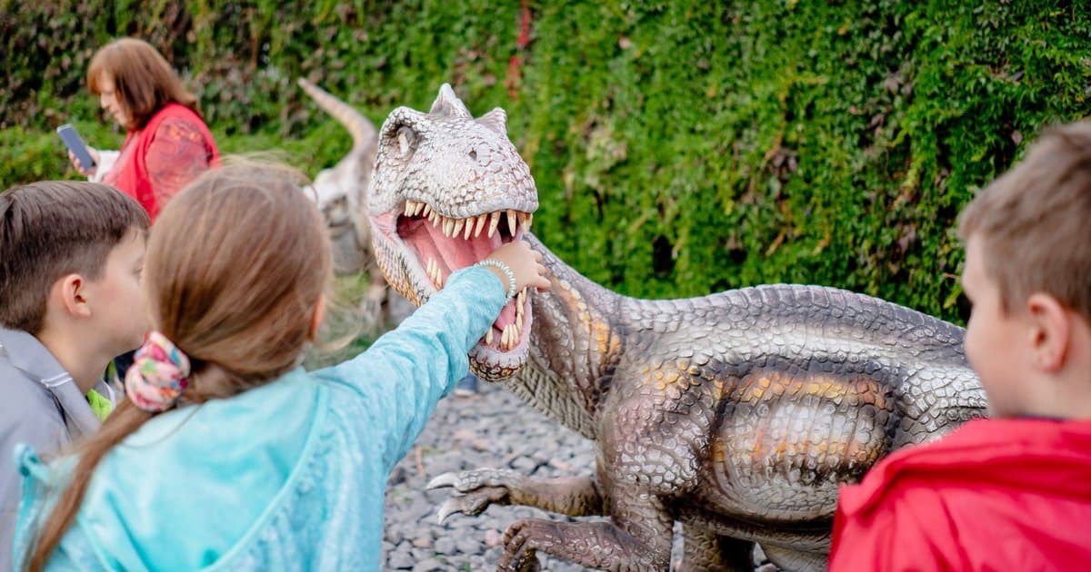 Children examining a large dinosaur model at an outdoor museum, one of many hands-on activities to engage kids with paleontology.