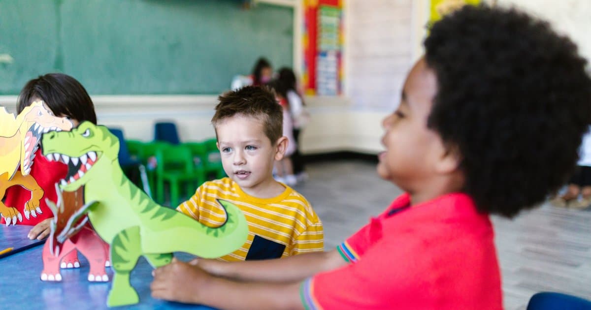 Children playing with dinosaur cutouts in a classroom, exploring hands-on learning activities.