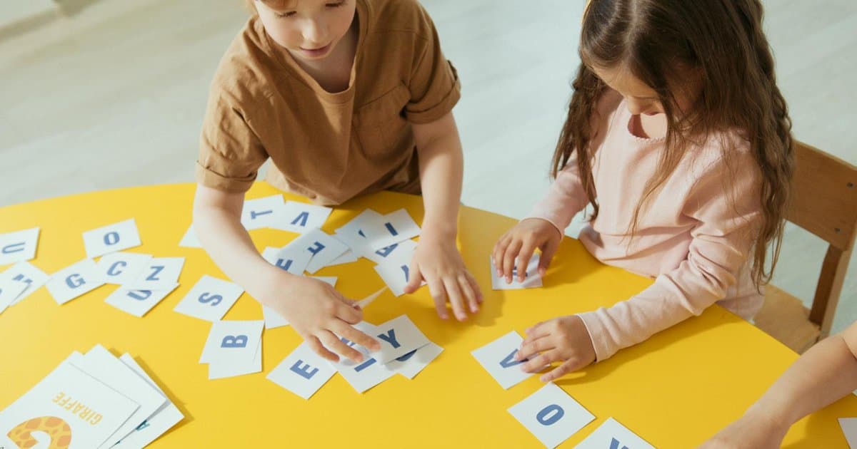 Two children make alphabet cards at a yellow table, demonstrating a hands-on learning project.