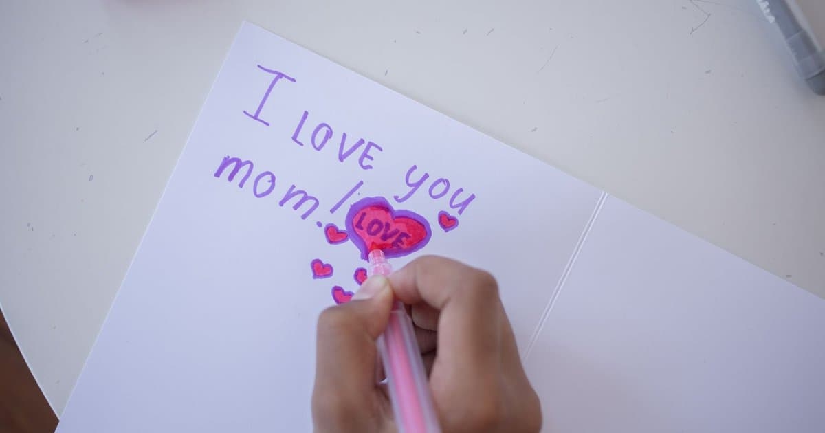 Child drawing in a greeting card with colored pens, representing handmade gift ideas for teacher appreciation.