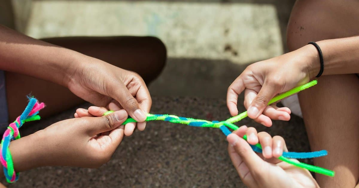 Children's hands weaving colorful yarn bracelets, an example of handmade gifts kids can make.