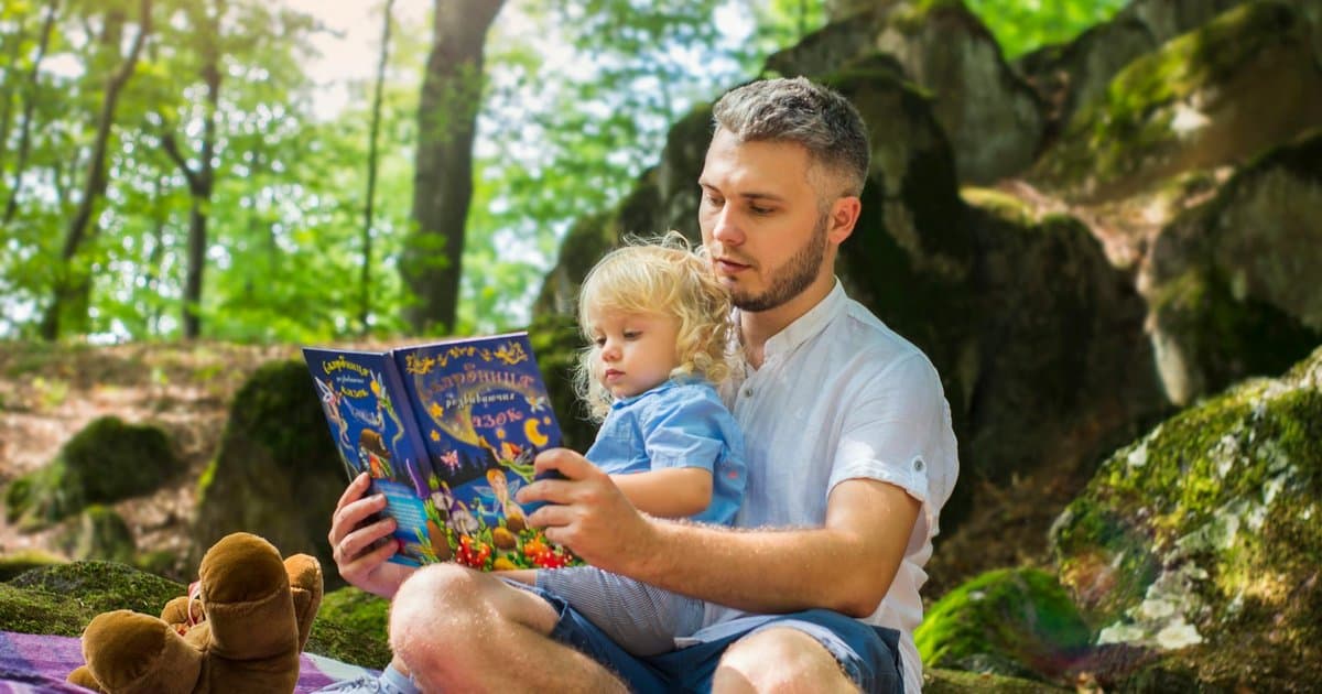 Father and toddler reading together in a sunny forest, illustrating the impact of quality children's books.