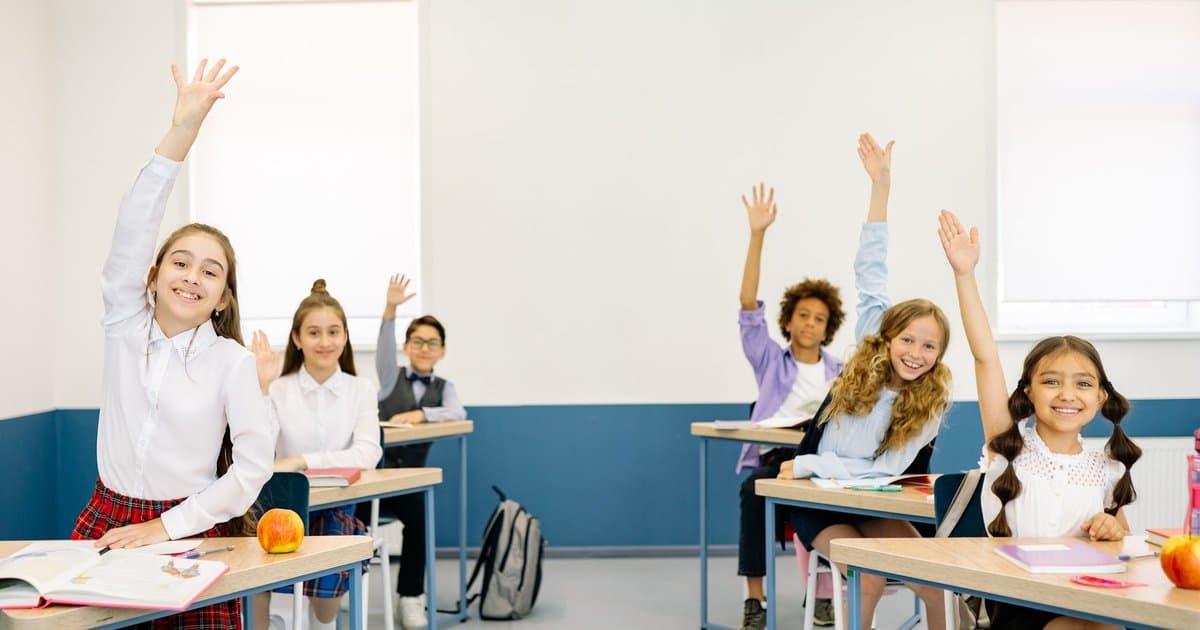 Diverse elementary students raising their hands in a classroom during Eid celebrations.