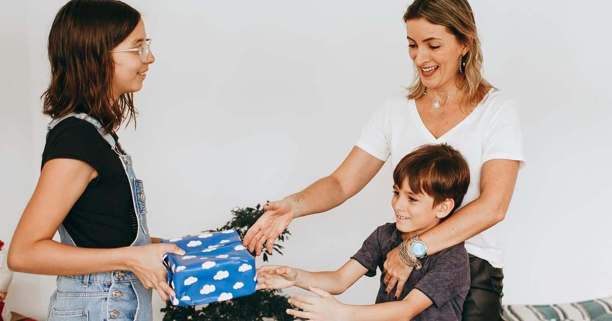 Children presenting a wrapped gift to their mother indoors, representing thoughtful end-of-year gifts for teachers.
