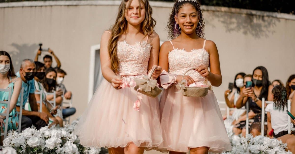 Two young flower girls in pink dresses walk down the aisle at a wedding ceremony.