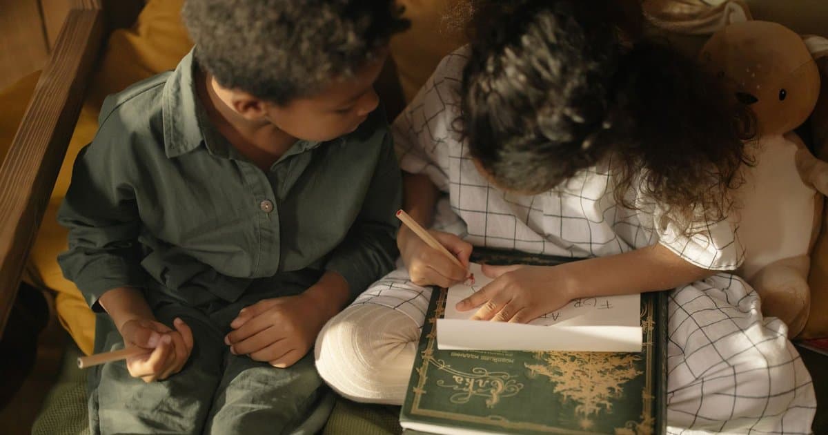 Two children drawing together indoors, creating imaginative stories through art and writing.