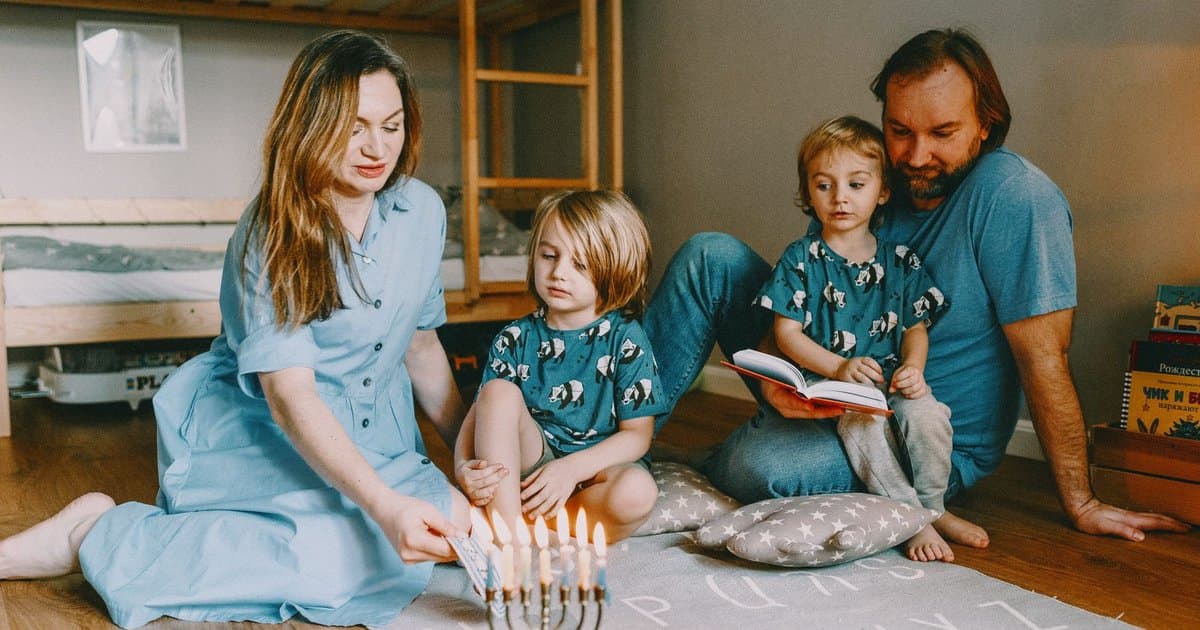 A family lights a menorah together at home, illustrating hands-on ways to engage children with Hanukkah stories.