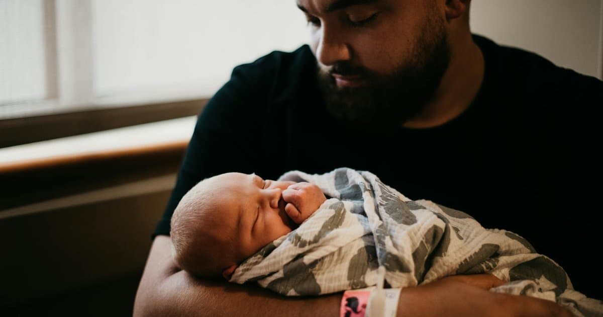 Father holding newborn baby wrapped in blanket, representing meaningful first Father's Day gifts for new dads.