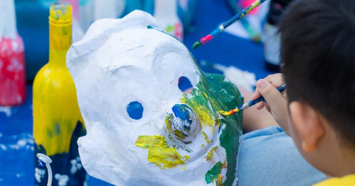 Children painting colorful masks at a table, demonstrating a DIY craft project teachers would enjoy.
