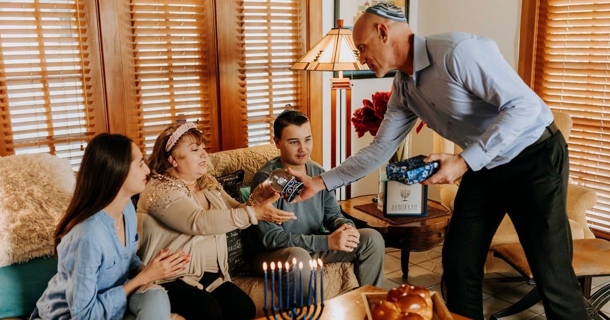A multigenerational family gathers around a menorah for Hanukkah, representing diverse ways families observe the holiday.