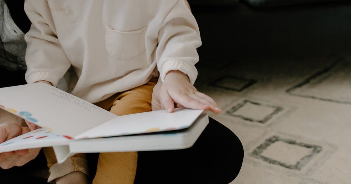 Toddler sitting on carpet reading a colorful picture book, exploring early literacy through engaging stories.
