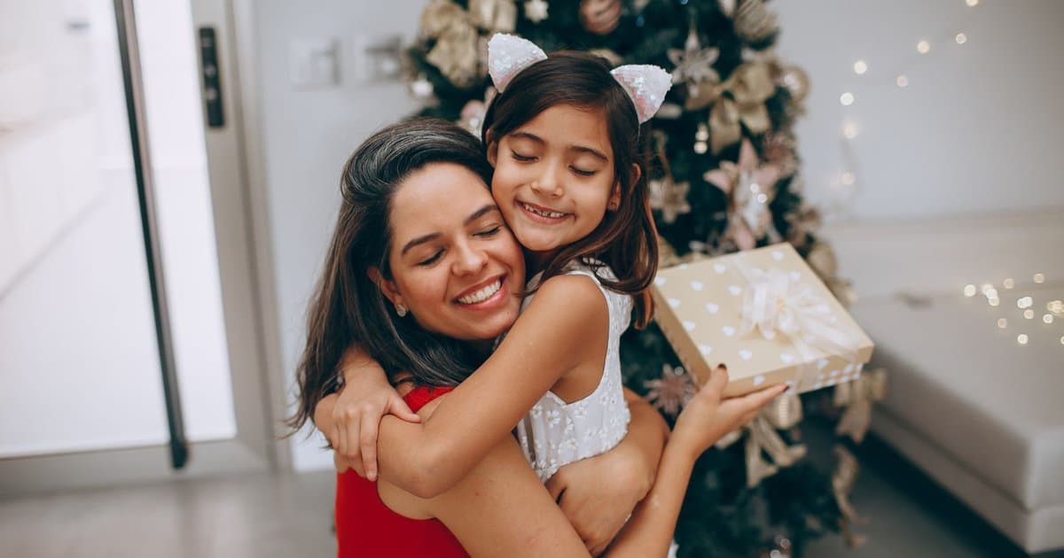 Mother and daughter hugging by a Christmas tree, representing handmade gift ideas with personal meaning.