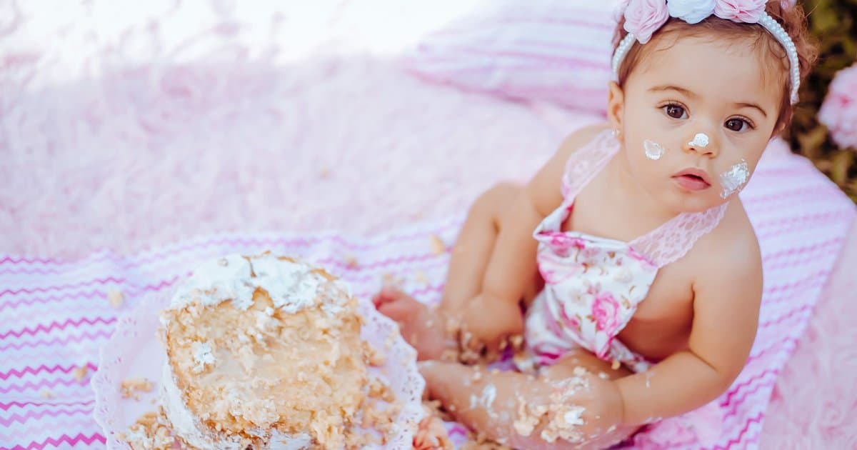 Baby eating cake outdoors on a blanket during first birthday celebration, demonstrating a memorable milestone to document in a keepsake book.