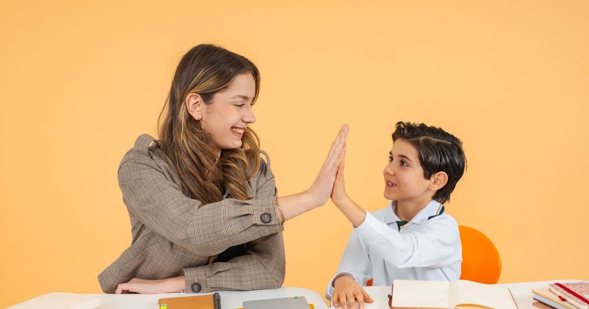 Teacher and student high-fiving at a desk, demonstrating positive reinforcement for classroom behavior.