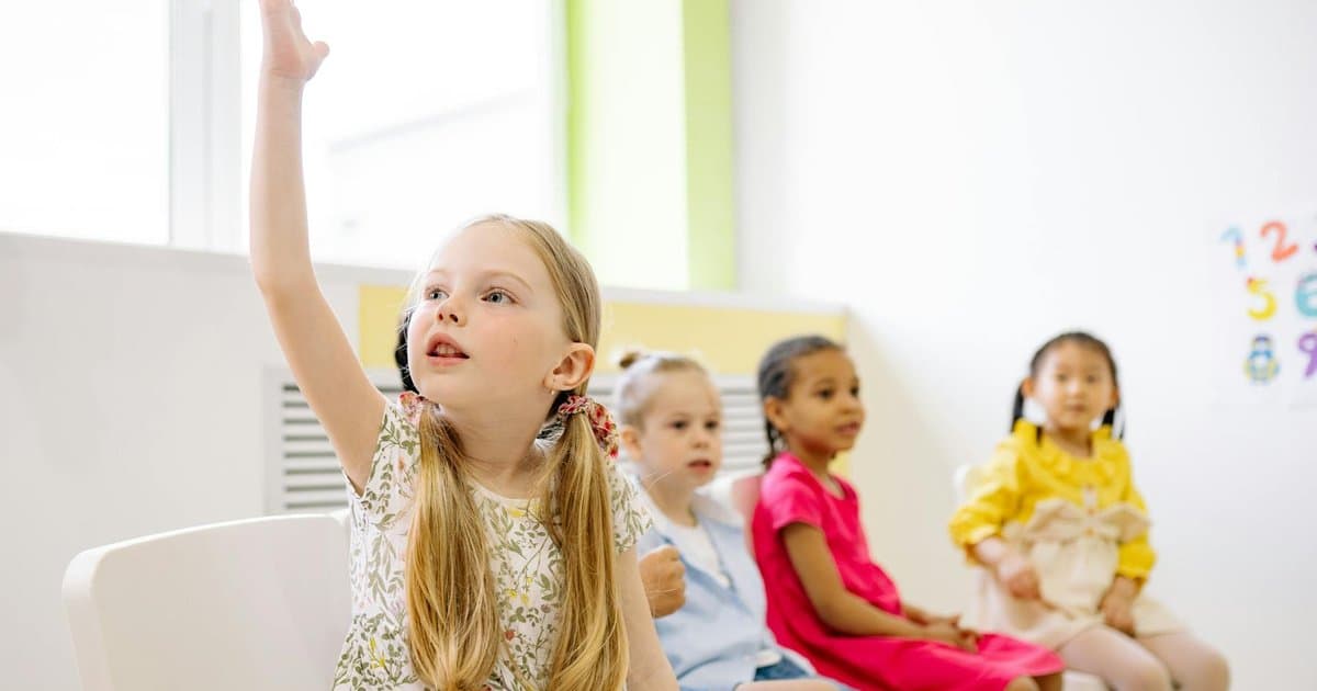 Kindergarten students raising hands in class, illustrating the memorable moments to capture in a classroom memory book.