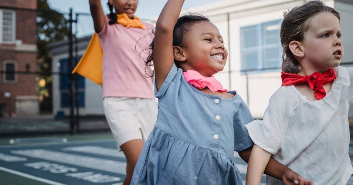 Three children playing superheroes outdoors, demonstrating cooperative play that builds social skills.