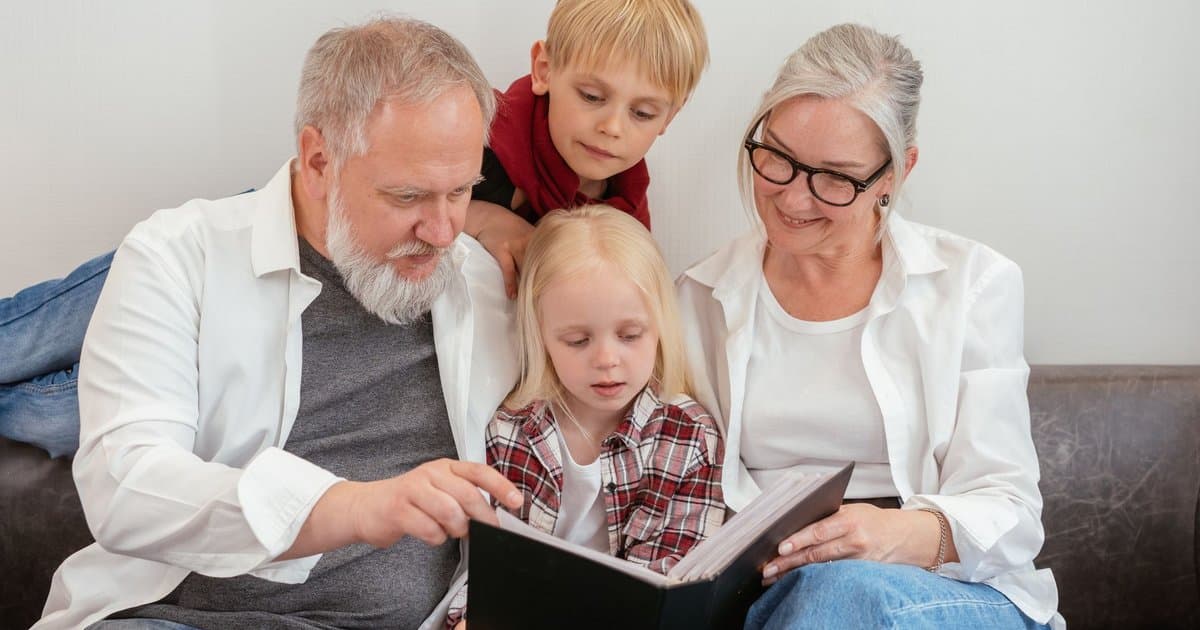 Grandparents and grandchildren review a photo album together, illustrating how to preserve family stories across generations.