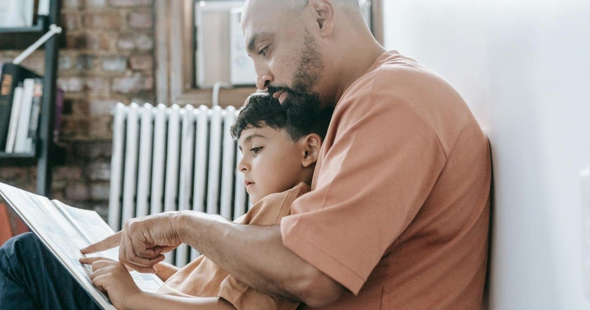 A father and son reading together at home, illustrating how teachers impact young learners.