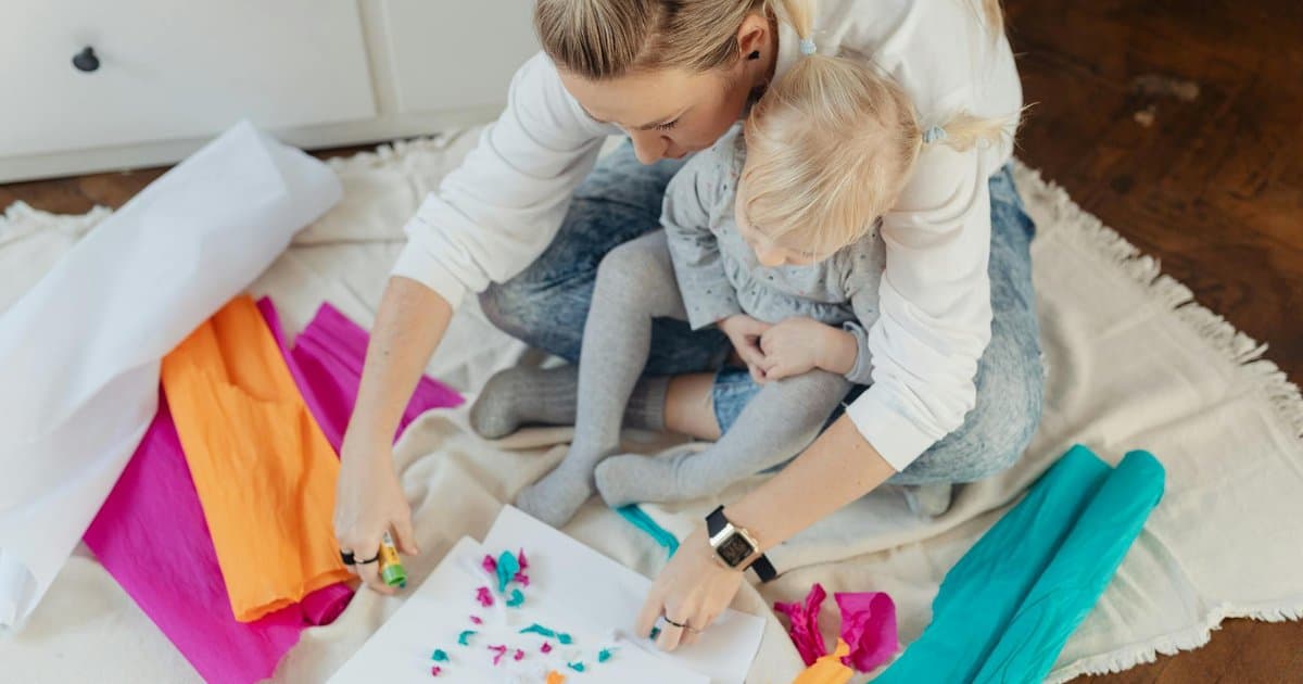 A mother and child work on a craft project together at a table with colorful materials.