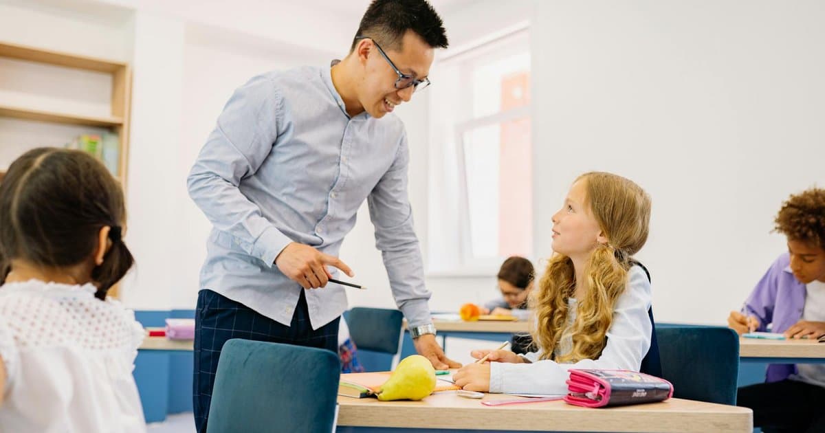 Male teacher helping diverse students in a bright classroom, illustrating practical teaching scenarios for gift-giving.