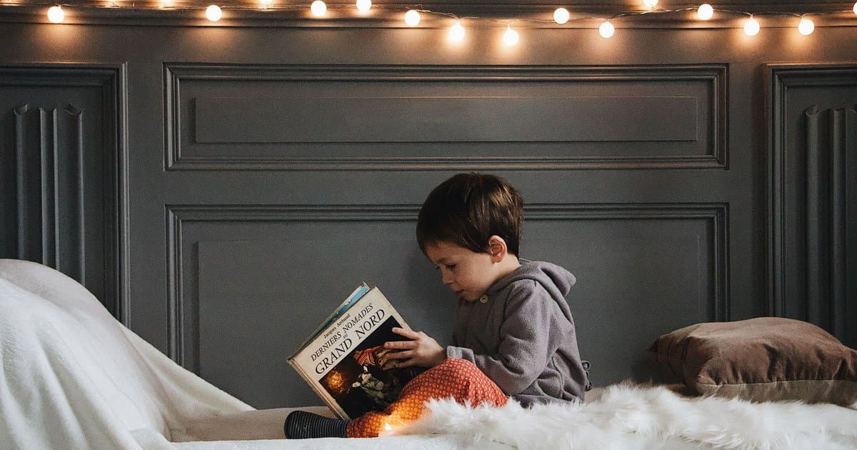 Young boy reading a book in a cozy bedroom with string lights, exploring how personalized storybooks impact early literacy.