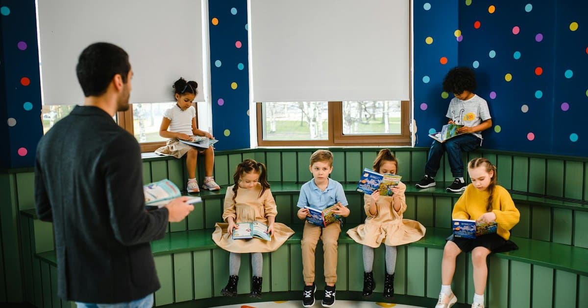 Teacher reads a customized alphabet book to a group of children sitting together in a classroom.