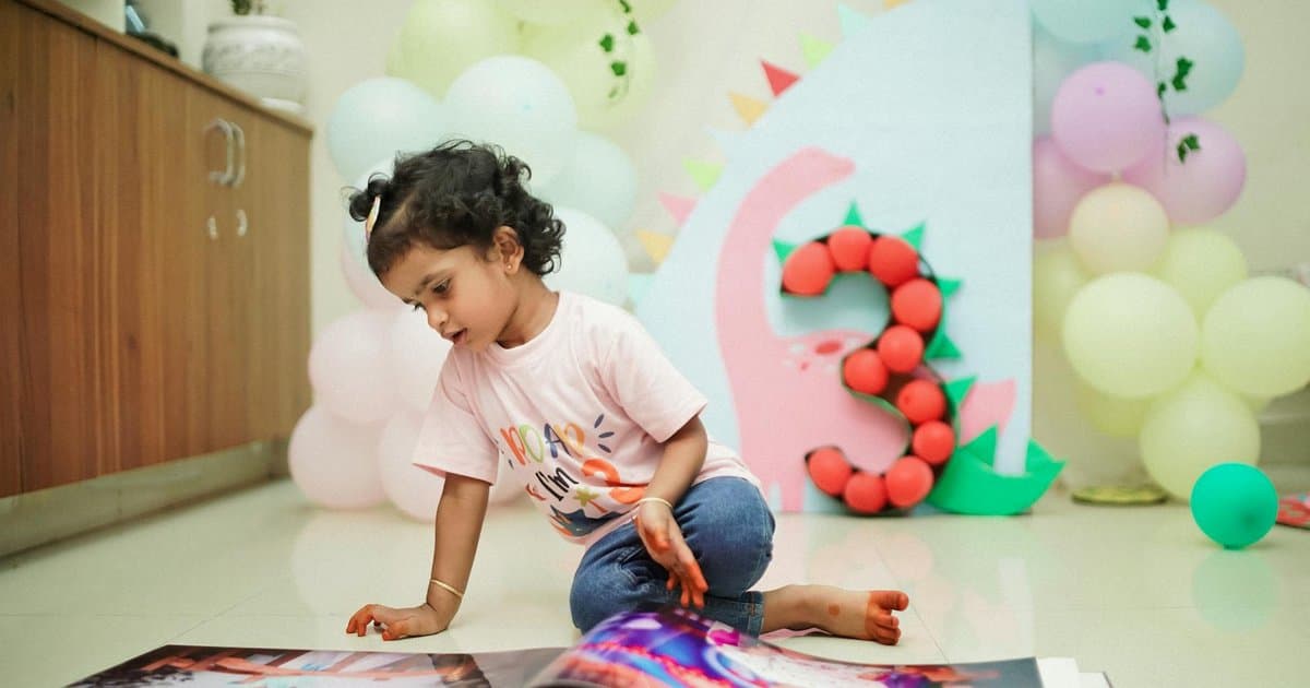 Toddler reading a personalized birthday newspaper book at a dinosaur-themed third birthday party.