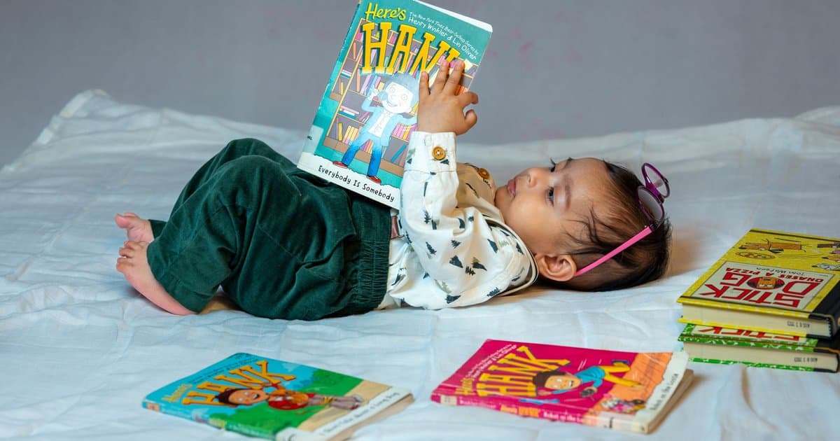 A 1-year-old reads colorful board books on a bed, examining the value of personalized books for toddlers.