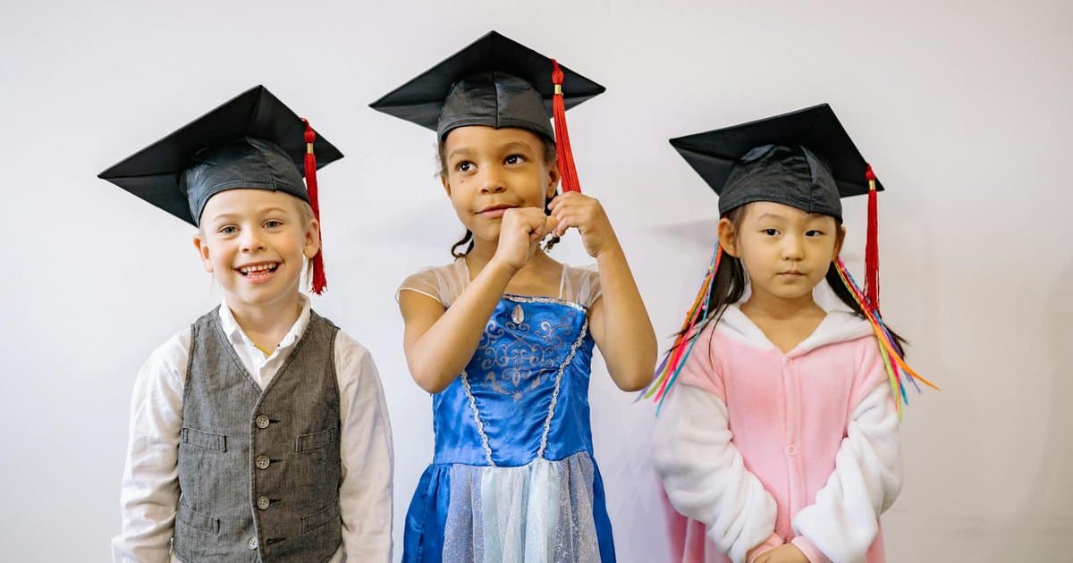 Three children in graduation caps smile at their preschool ceremony, celebrating a milestone moment worth marking with meaningful gifts.