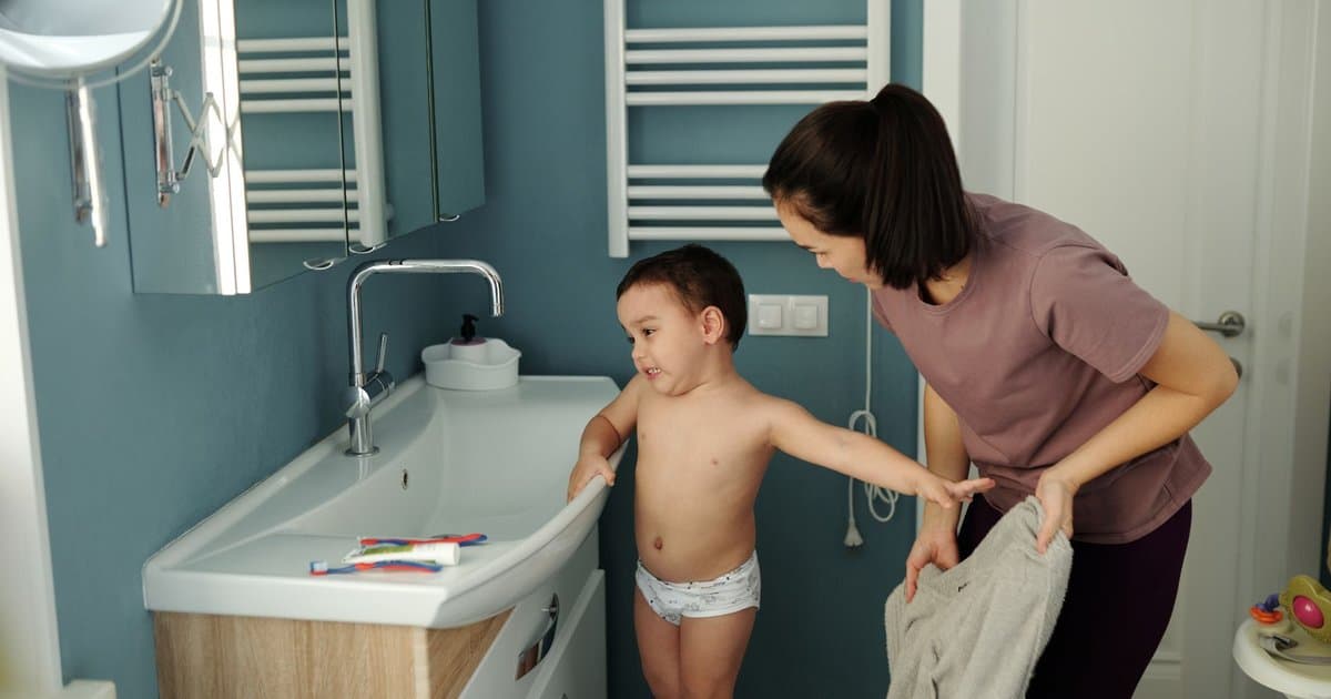 A mother assists her young son at the sink during bathroom routines.