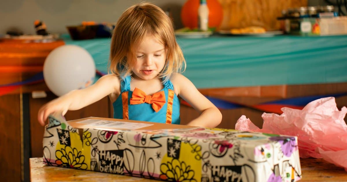 Young girl unwrapping a colorful gift at home, representing meaningful presents for preschool milestones.