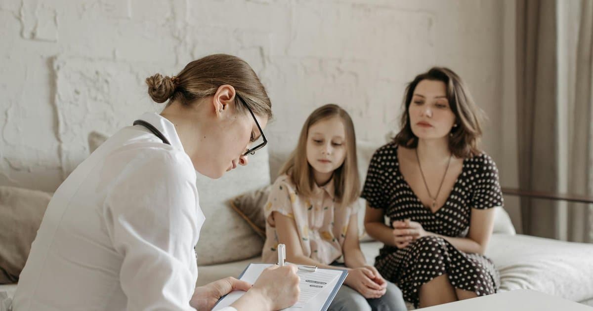 A doctor speaking with a mother and young girl in an exam room, illustrating a typical pediatric appointment visit.