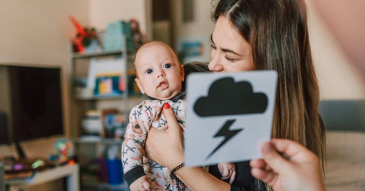 Mother showing a flashcard to her baby indoors, demonstrating an early learning activity with visual cards.