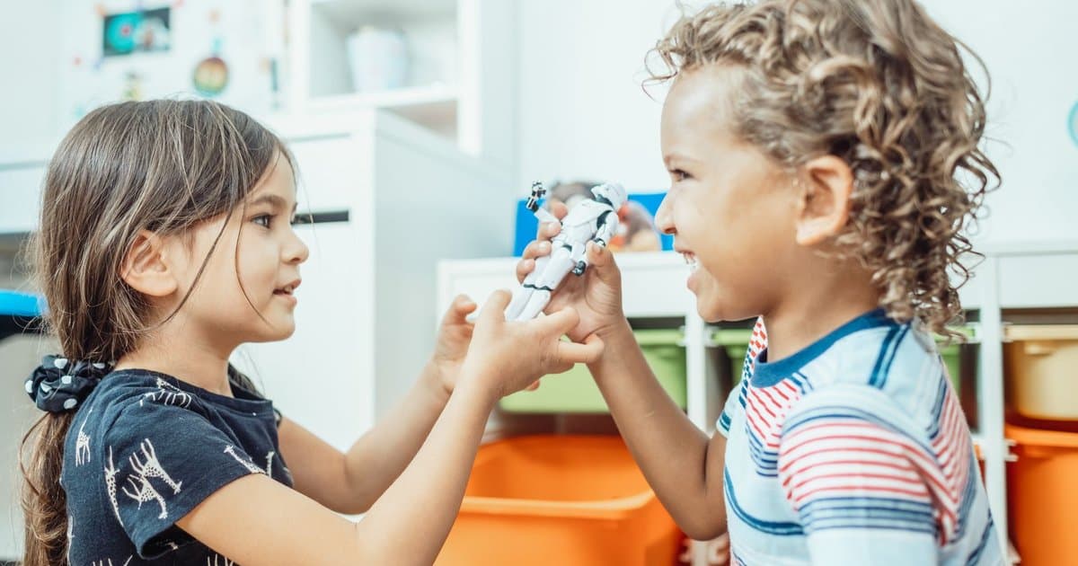 Two children playing indoors and sharing a toy, demonstrating sibling bonding and cooperation.