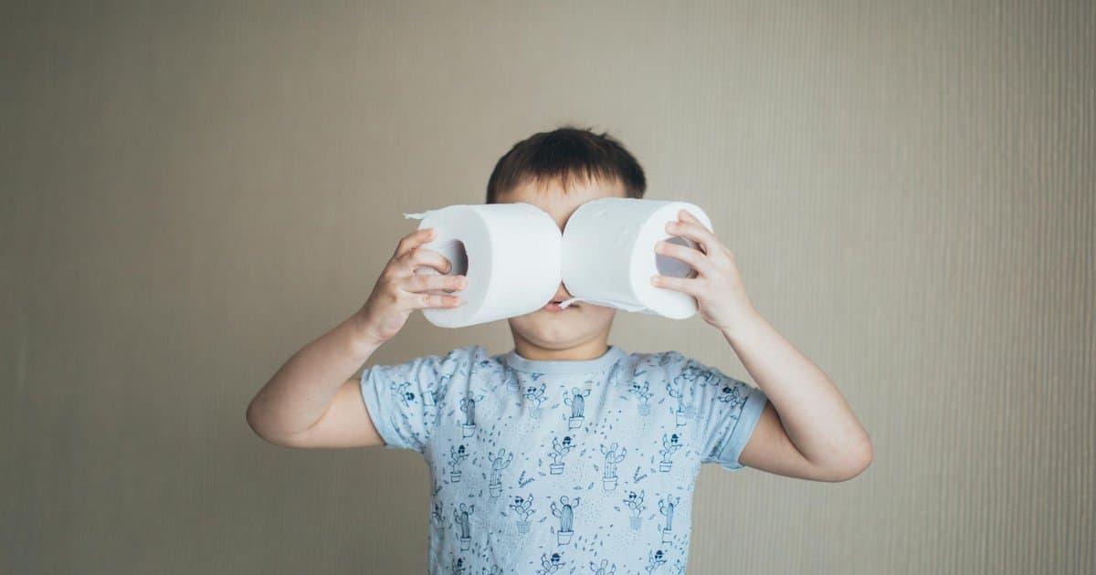Toddler boy playing with toilet paper rolls indoors, illustrating bathroom familiarity and readiness exploration.