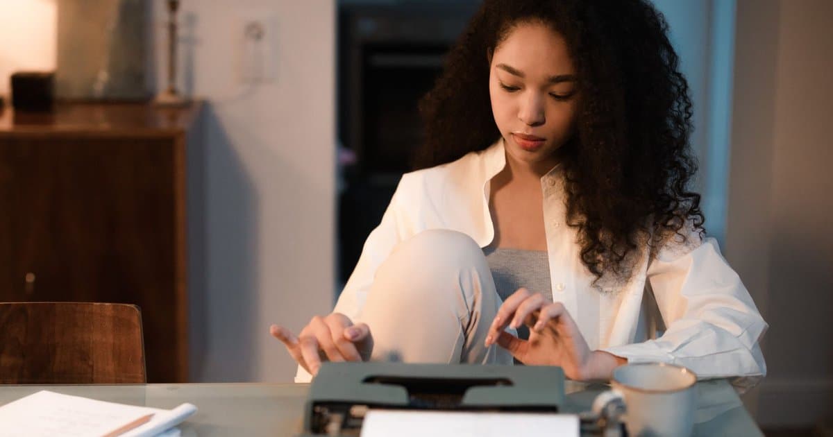 Young writer typing on vintage typewriter at desk, illustrating the writing process for crafting superhero origin stories.