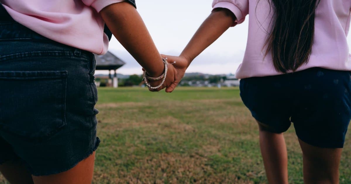 Two children holding hands in a park, demonstrating compassion and connection between peers.