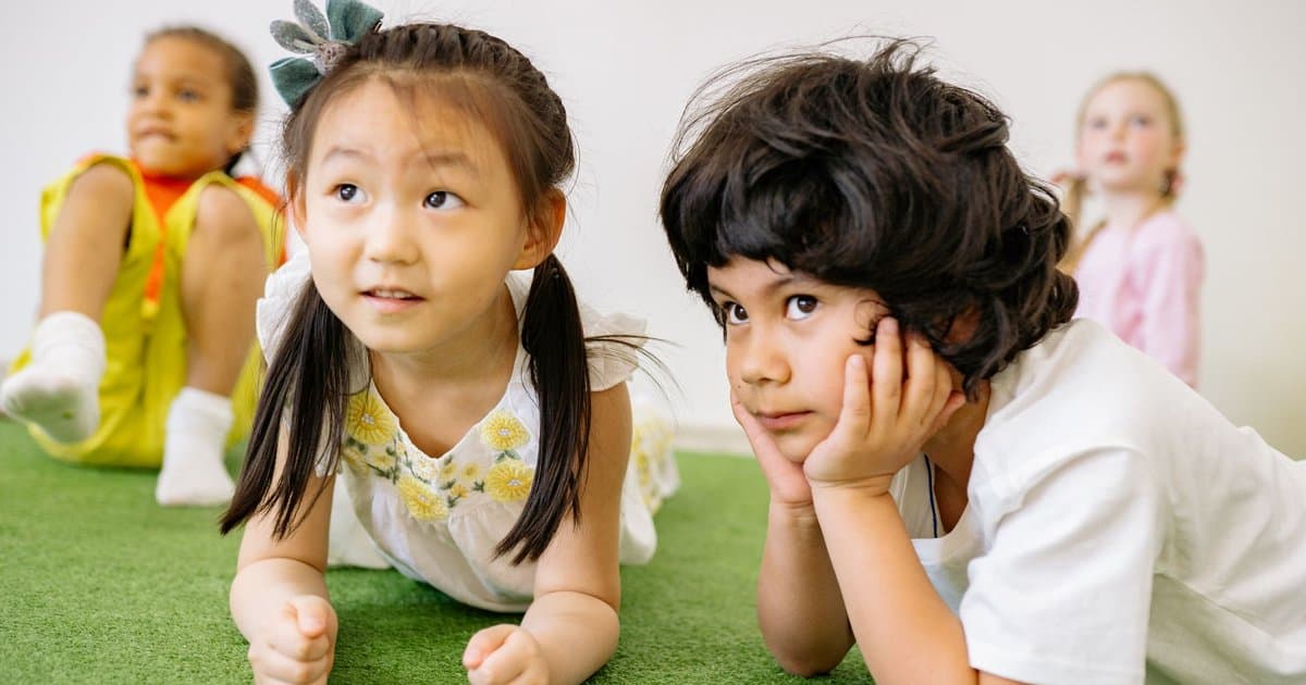 Children sitting together on grass during a group activity, illustrating collaborative learning and emotional connection.