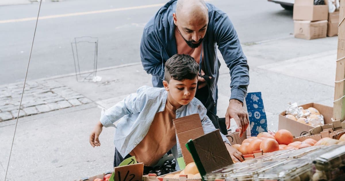 Father and son selecting fresh produce at a market, demonstrating grocery shopping skills for kids.