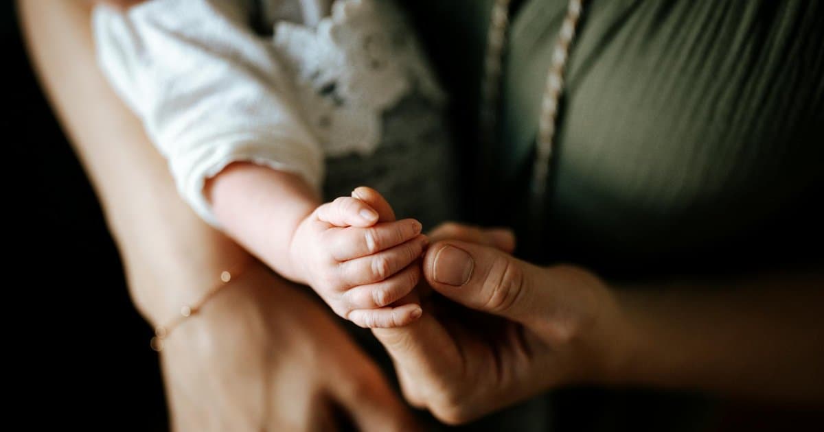 Mother holding her premature baby's hand in a hospital setting, illustrating neonatal care.
