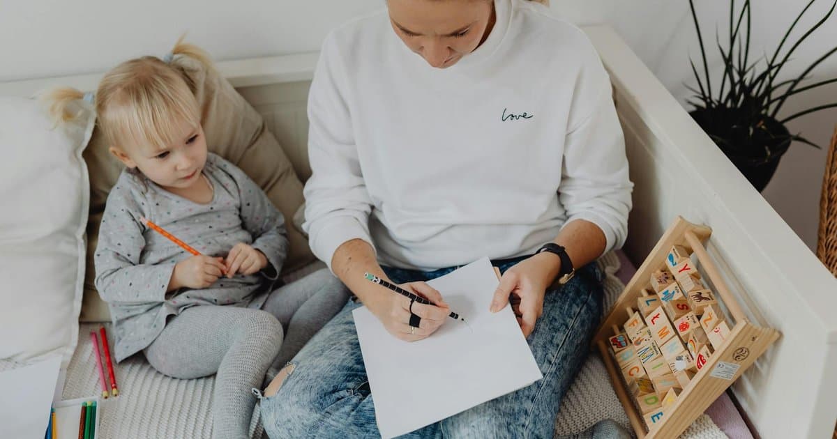 A mother and child work with alphabet blocks and colorful pencils, practicing letter recognition together.