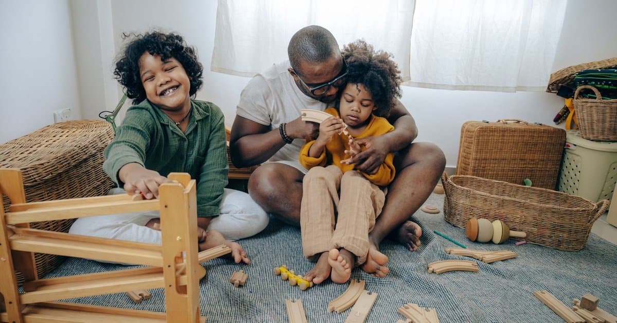 Father and daughters building with wooden blocks together, an example of screen-free indoor activity for kids.