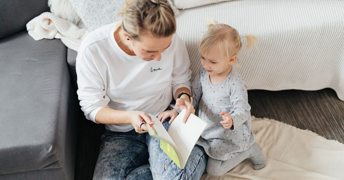Mother and daughter reading a book together in a living room, illustrating the use of social stories for potty training.
