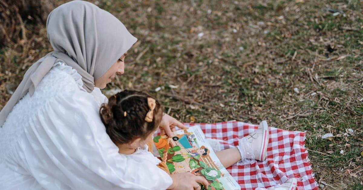 A mother and daughter read together on a picnic blanket, illustrating shared reading time used in potty training preparation.